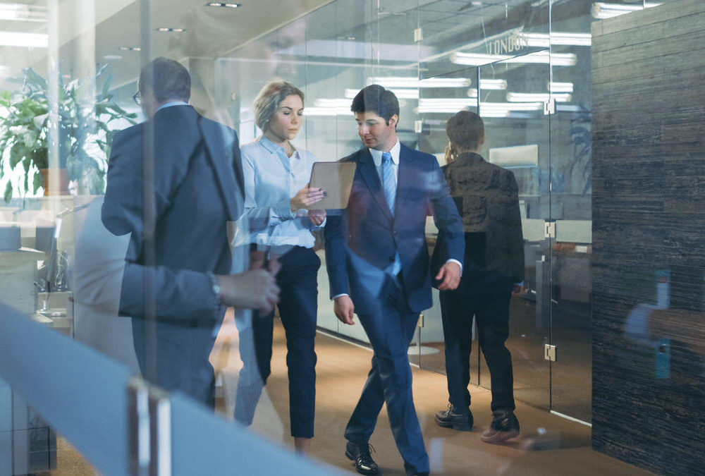 Businessman,And,Businesswoman,Walking,Through,Glass,Hallway,,Discussing,Work,And