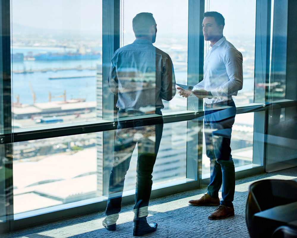 Two,Businessmen,Deep,In,Discussion,Together,While,Standing,By,Windows