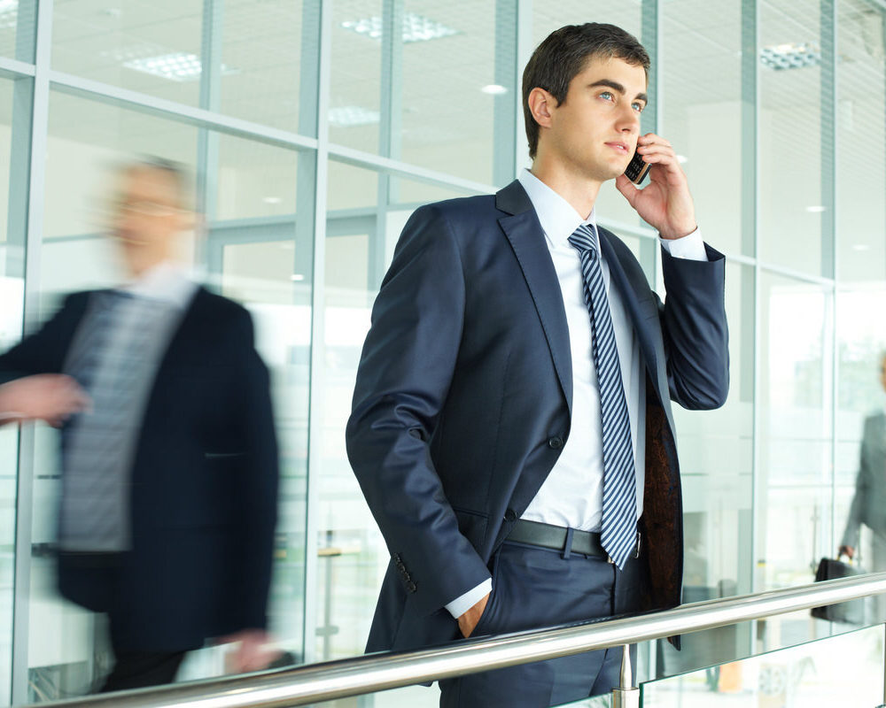 Businessman,Standing,By,Banisters,And,Calling,With,Walking,People,On