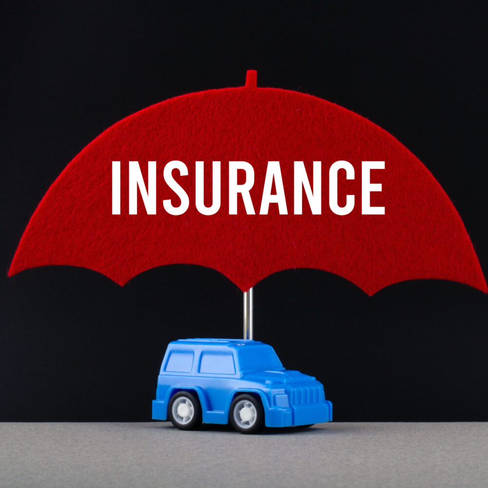 Concept of car insurance. Blue car under red umbrella with text Insurance