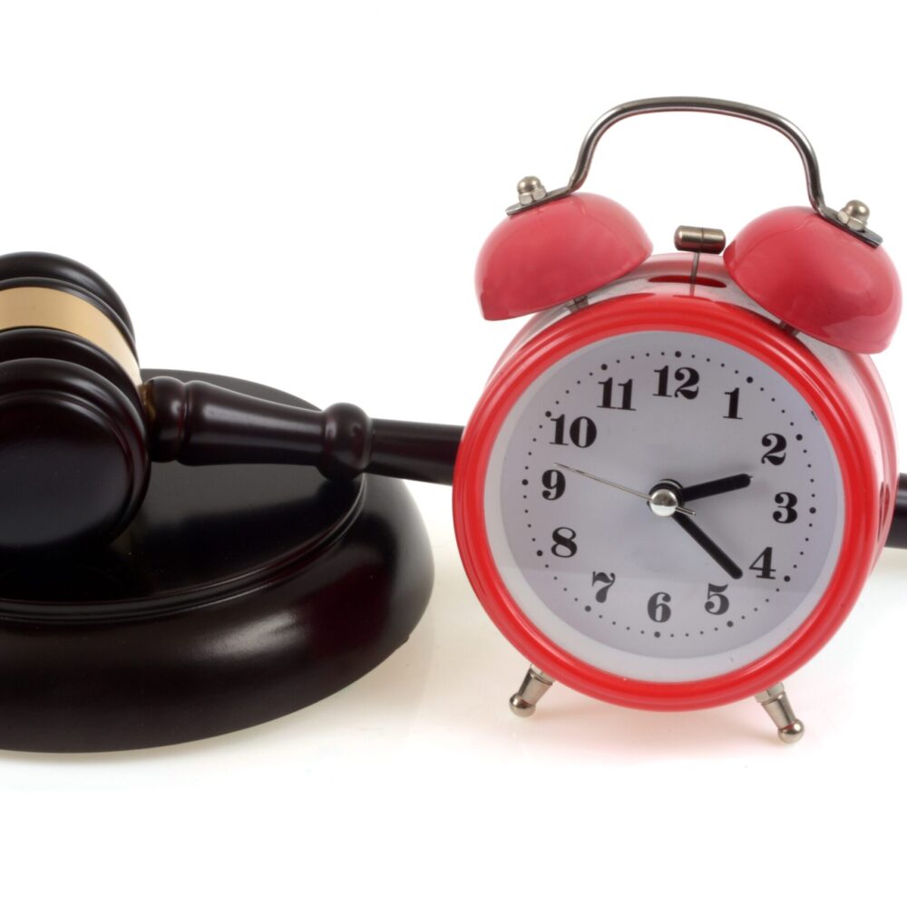 Judge's gavel on its plinth next to a bell clock in close-up on white background